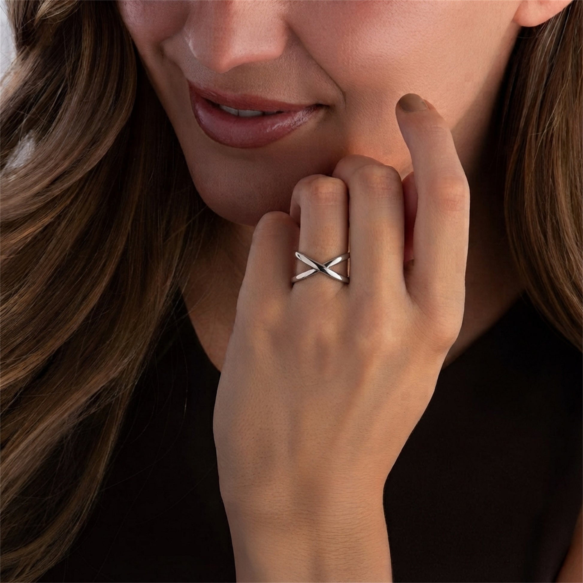 Silver criss-cross love knot ring on finger near chin, model wearing it.