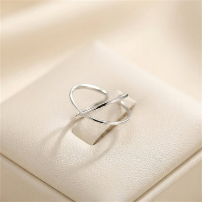 Silver criss-cross love knot ring with crossed bands on a light surface.