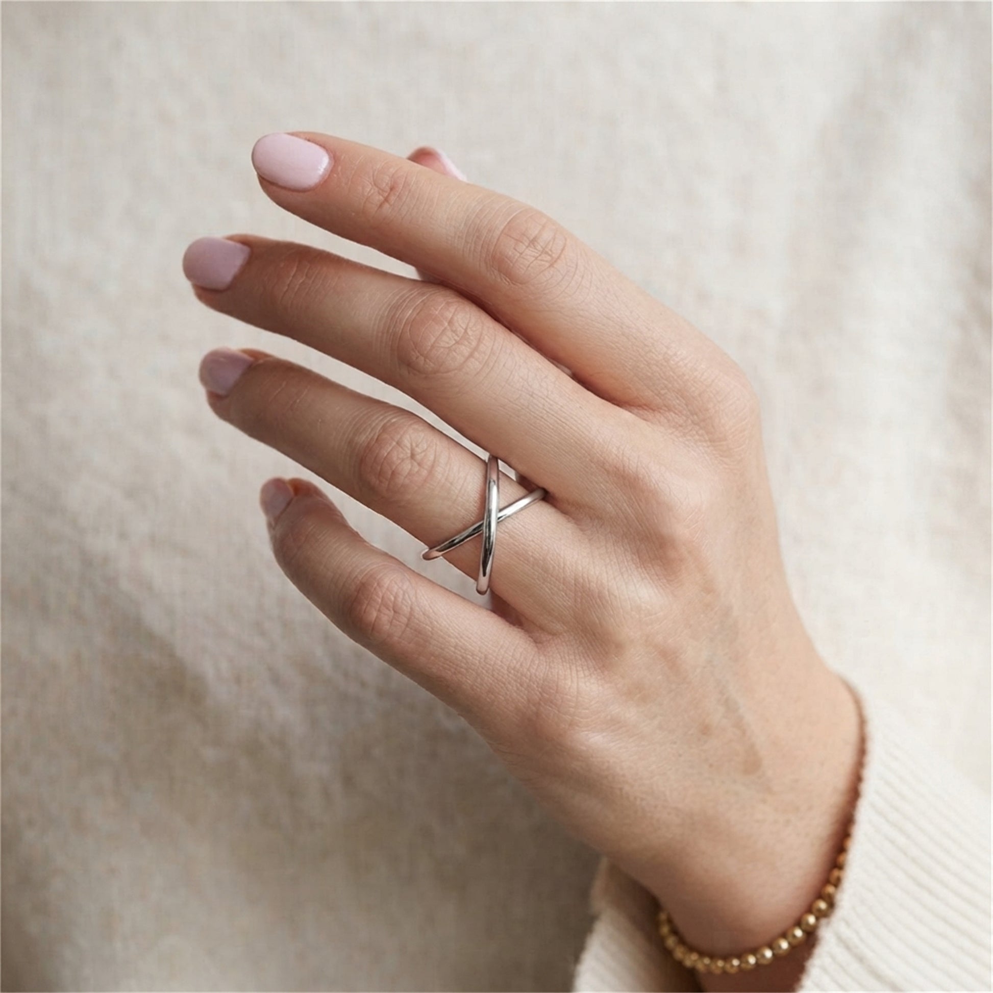 Criss-cross love knot ring on finger, silver interwoven band design.