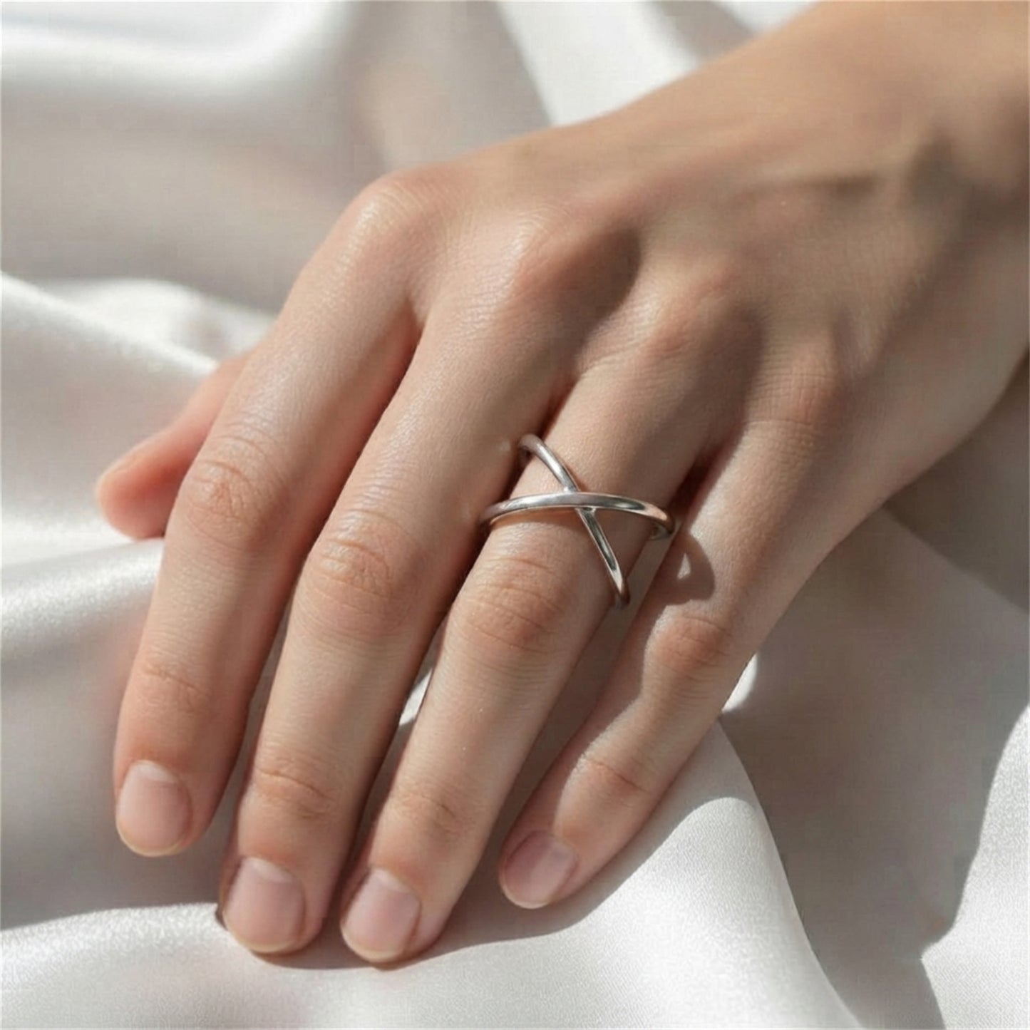 Silver criss-cross love knot ring on finger over white fabric.