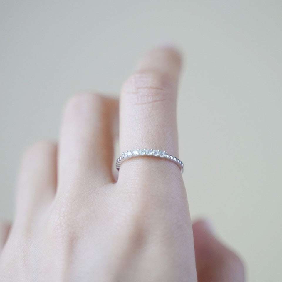Silver half-eternity beaded ring with clear stones, worn on finger.