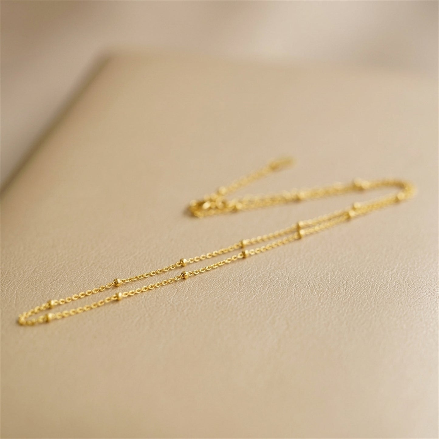 Gold beaded satellite chain necklace close-up, delicate flat links with bead accents.