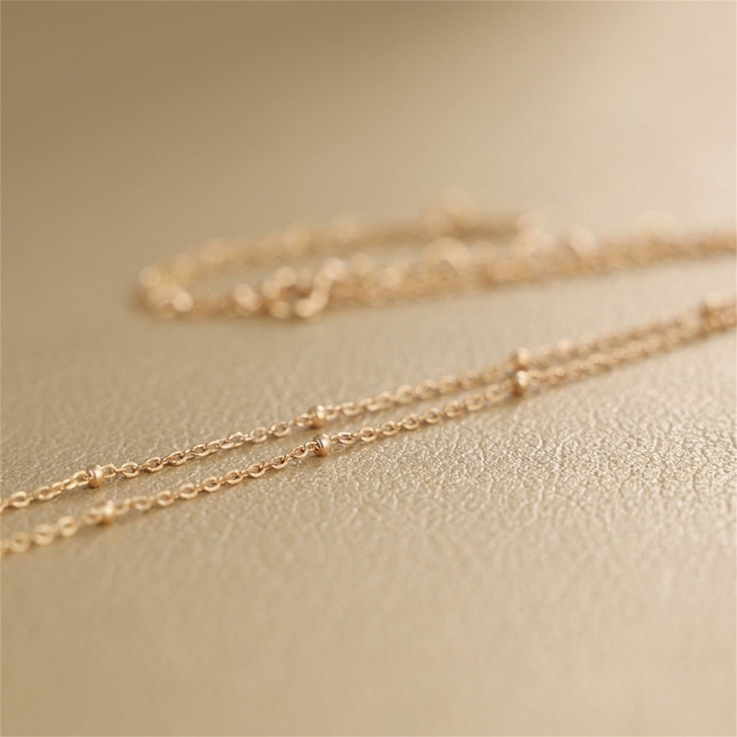 Gold beaded satellite chain necklace close-up, tiny round beads along flat links.