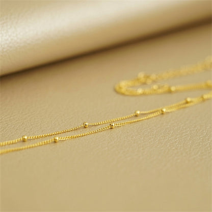 Gold beaded satellite chain necklace, small round bead links in a flat line.