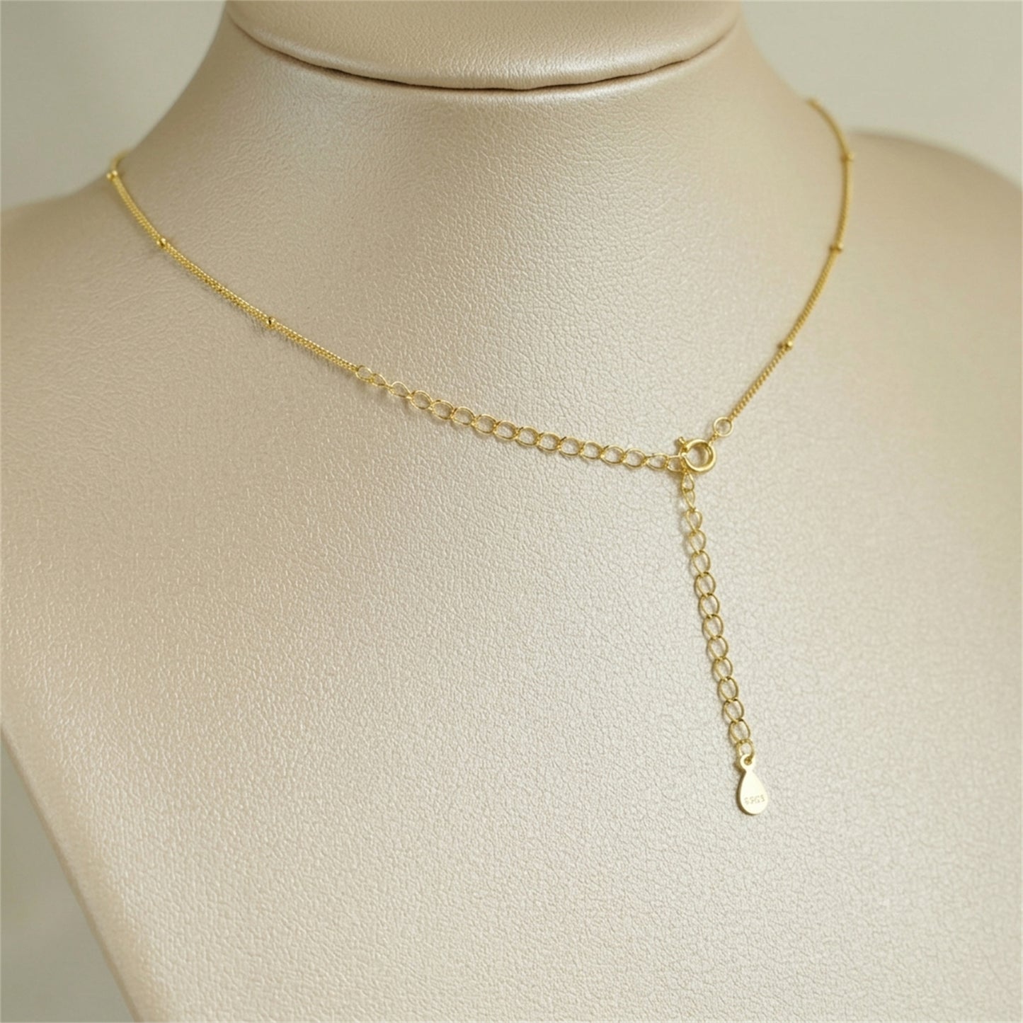 Gold beaded satellite chain necklace with short drop pendant and clasp ring.