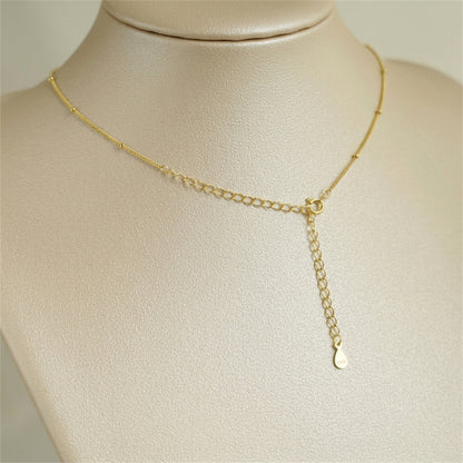 Gold beaded satellite chain necklace with short drop pendant and clasp ring.