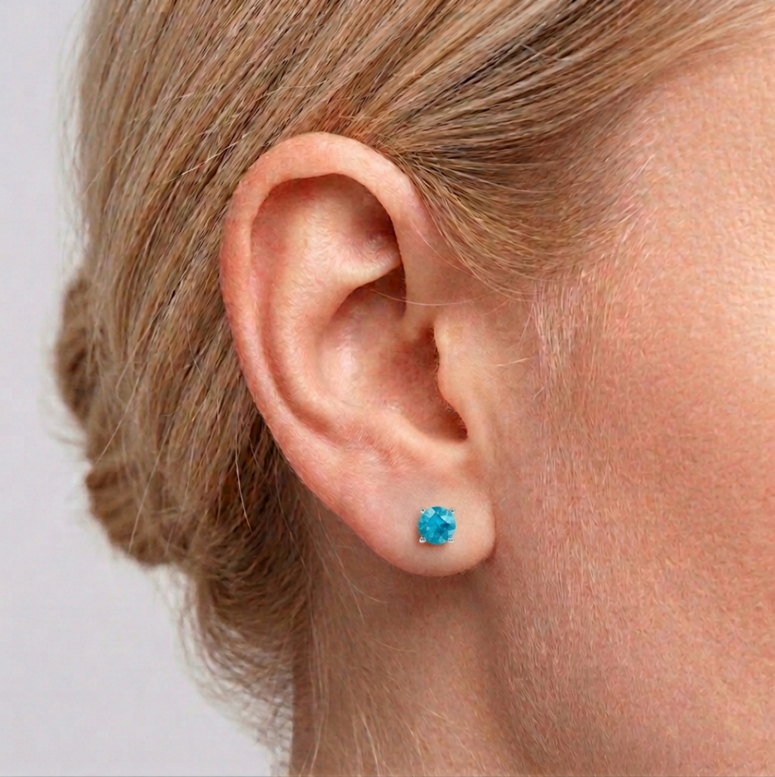 Round CZ solitaire stud earrings on ear with small light blue round stone