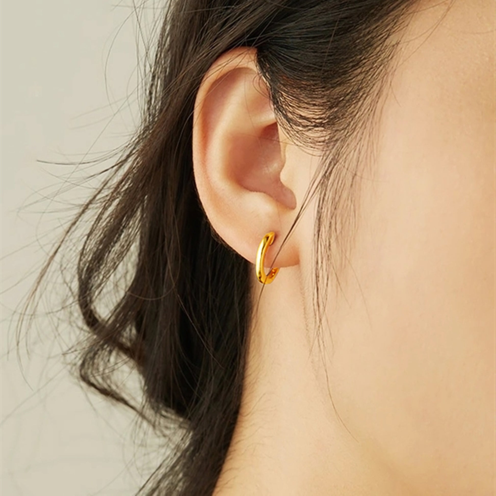 Small gold hoop earrings with latch-back clasp on ear
